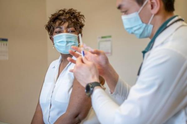 A doctor prepares to inject a senior woman's arm with a dose of vaccine.