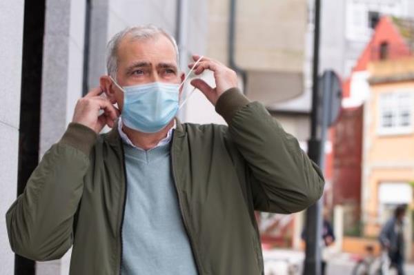 A senior man putting on a face mask in public