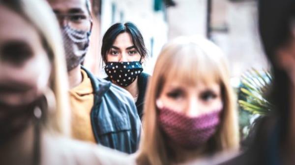 commuter crowd of people moving on city street covered by face mask - New normal human co<em></em>ndition and society co<em></em>ncept - Focus on middle woman wearing black facemask - Desaturated co<em></em>ntrast filter