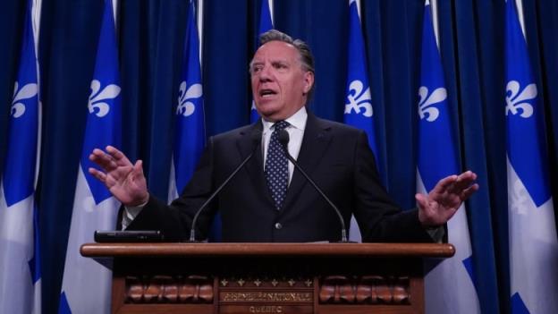 A man speaking at a podium in front of Quebec flags. 