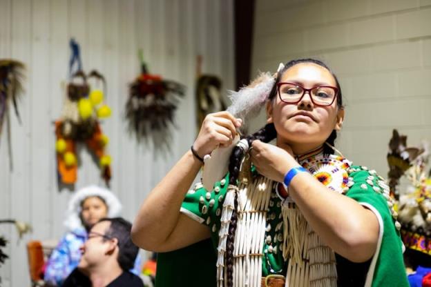 A young girl ties a hair piece to her powwow regalia.