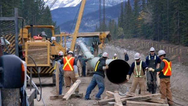 A group of men wearing safety vests handle a piece of pipe for the Trans Mountain pipeline expansion.