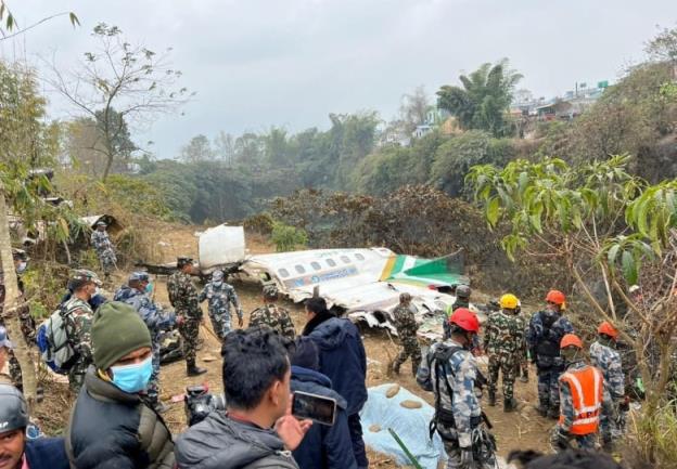 Part of a plane's fueselage is seen on the ground in a jungle setting, while rescuers in helmets and masks look on.