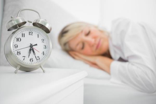 Woman sleeping in bed next to an alarm clock on a table.