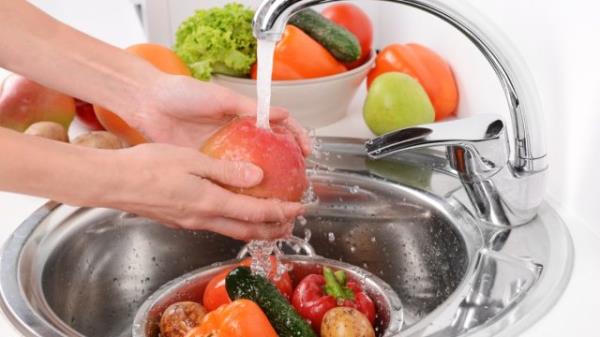 person washing fruits and vegetables in a me<em></em>tal kitchen sink