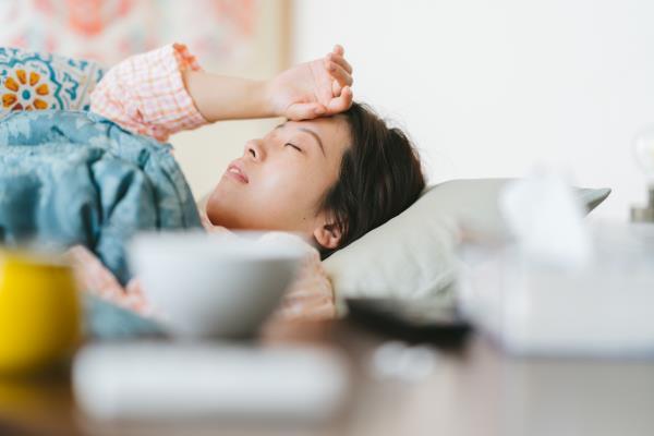 A sick woman lying on her sofa and covering her forehead with her hand