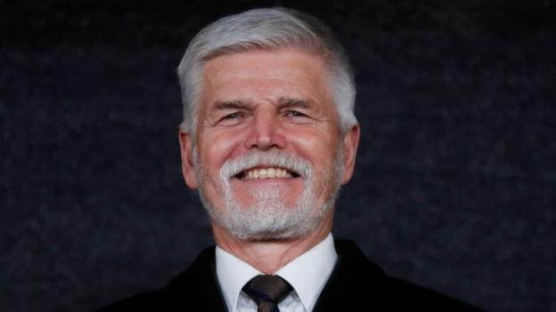 A silver-haired man wearing a dark suit smiles.