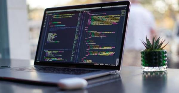 A MacBook Pro on a black desk shows lines of code.