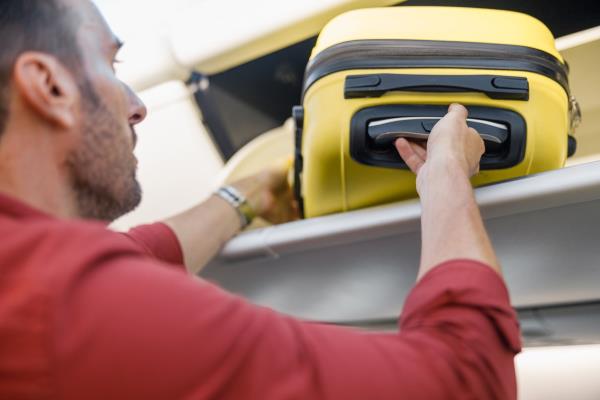 Man pulling out hand luggage from compartment while traveling by plane. Vacation, transportation concept