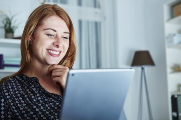 Woman smiling as she reads through co<em></em>ngratulations messages on her laptop