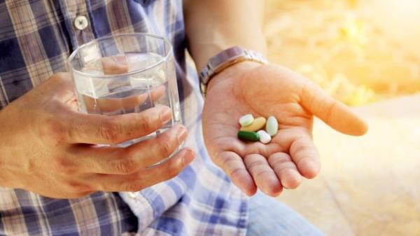 A senior man holding vitamins and supplements in this palm with a glass of water