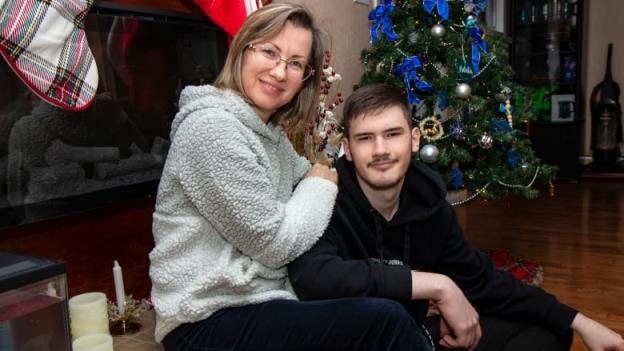 A woman and her teenage son sit in front of a Christmas tree.