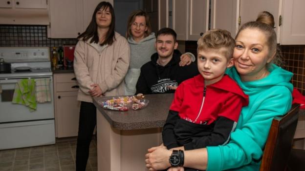 A group of five people sit and stand in a kitchen.