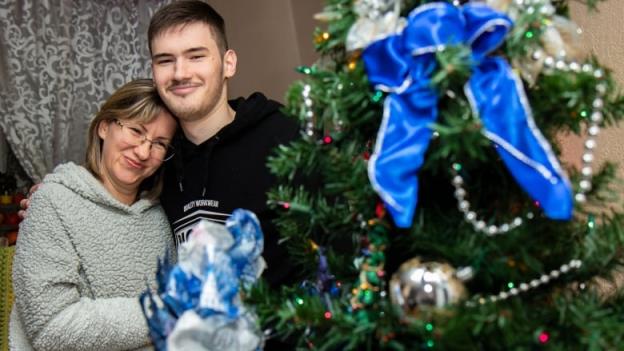 A woman and her son stand by a Christmas tree.