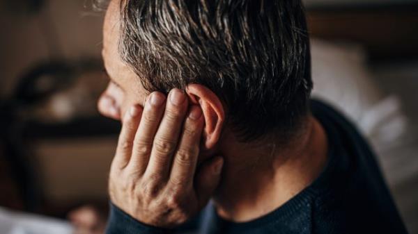 A middle-aged man touching his ear maybe suffering from hearing loss