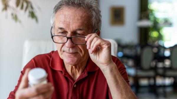 white-haired man reading supplement label