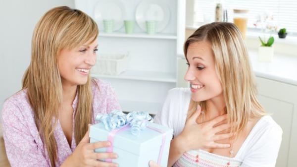 woman looking happy and surprised while friends gives her a big box with a bow on top