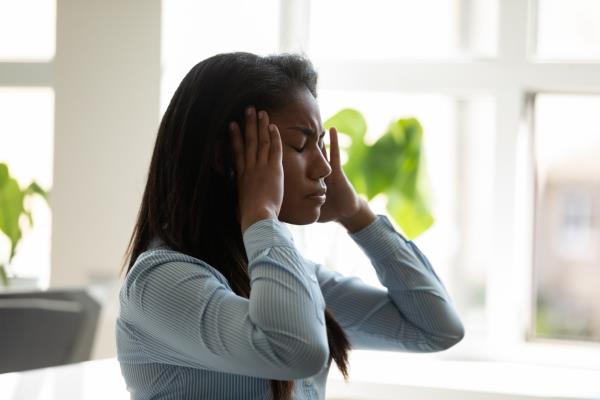 Unhappy african american businesswoman suffering from headache at work at laptop. Diverse female employee stressful touching temples holding head thinking a<em></em>bout business problem.