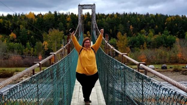 A woman raises her hands in happiness as she stands on a suspension bridge.  