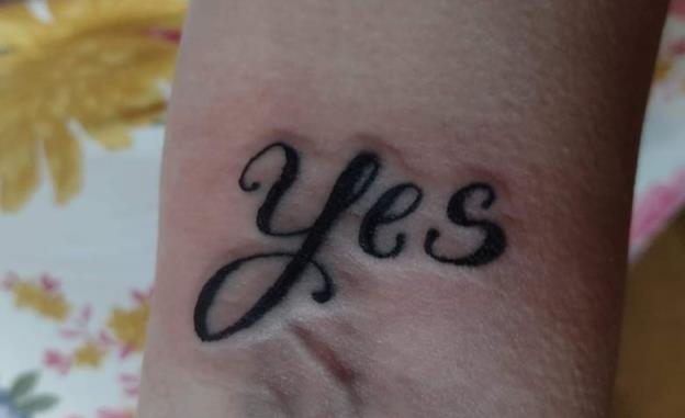 A freshly-inked tattoo of the word “Yes” on a woman’s forearm. 